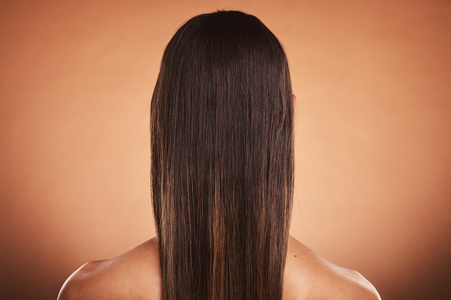 Brunette woman, shine and hair care, beauty salon, balayage and hair dye, color cosmetics and wig extension on studio orange background. Back of head, scalp and long hair style with smooth texture.